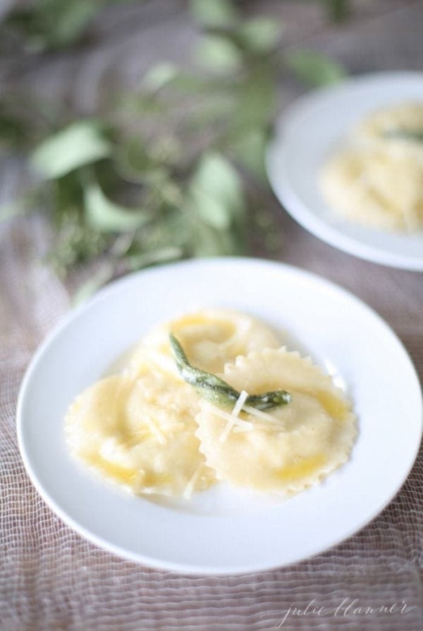 wonton ravioli in butter sage sauce on a white plate with sage leaves in background