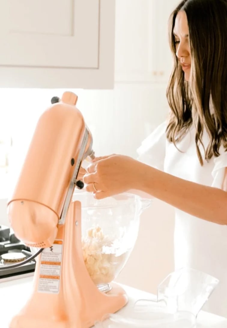 A woman is preparing food in a kitchen with a pink mixer.