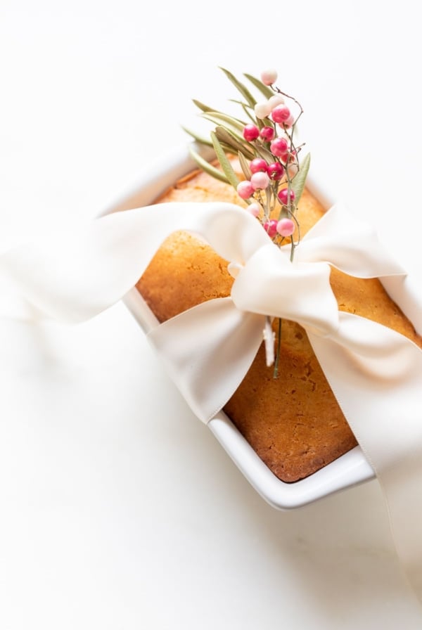 Almond bread in a white loaf pan tied with a white satin bow and a touch of pink berries.