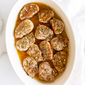 Apple cider pork tenderloin medallions in a white baking dish.