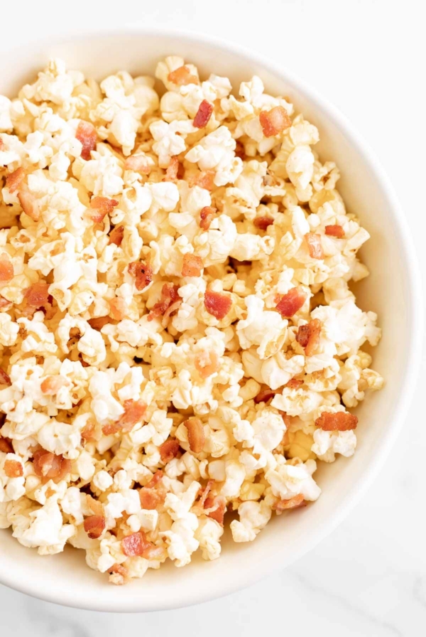 A white bowl filled with popcorn with bacon pieces