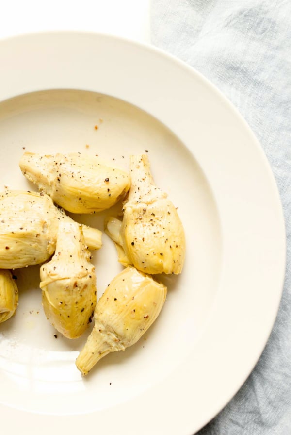 baked artichoke garnished with parmesan in cream serving bowl