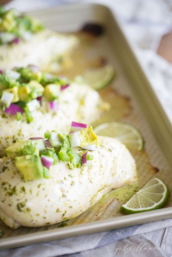 simple avocado salsa on top of chicken breasts on baking sheet with lime wedges