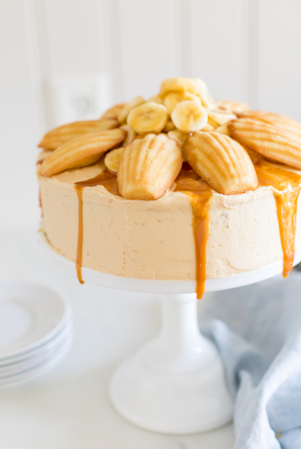 A round banana cake topped with madeleine cookies and caramel sauce.