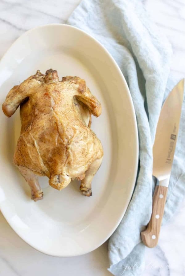 White platter featuring a beer can roasted chicken with golden skin. Blue linen napkin to side. #beercanchicken