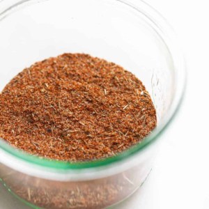 White surface, small glass bowl full of blackened chicken seasoning blend.