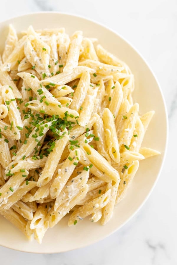 A white serving bowl full of Boursin pasta topped with chives.