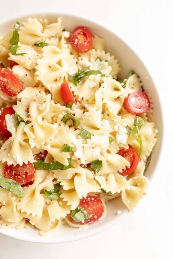 bow tie pasta salad in a bowl with cherry tomatoes basil and feta