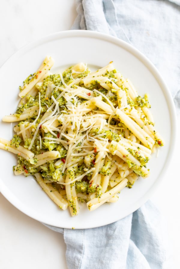 A white plate filled with broccoli pasta, blue napkin behind.