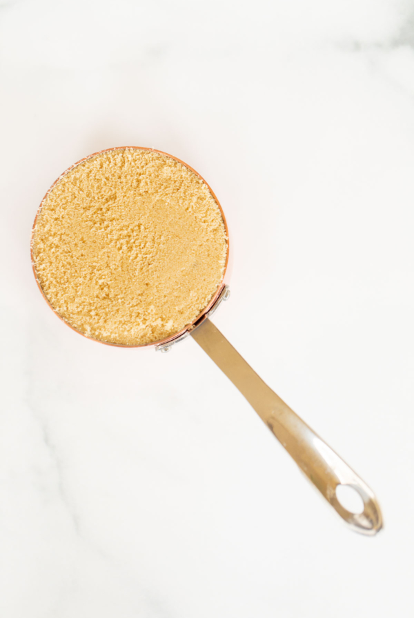 Light brown sugar in a copper measuring cup on a marble countertop.