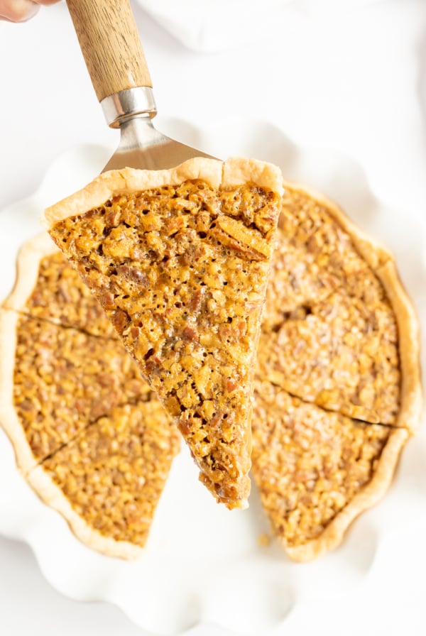 A person cutting a piece of a pie with a spatula and enjoying the delicious caramel pecan pie recipe.