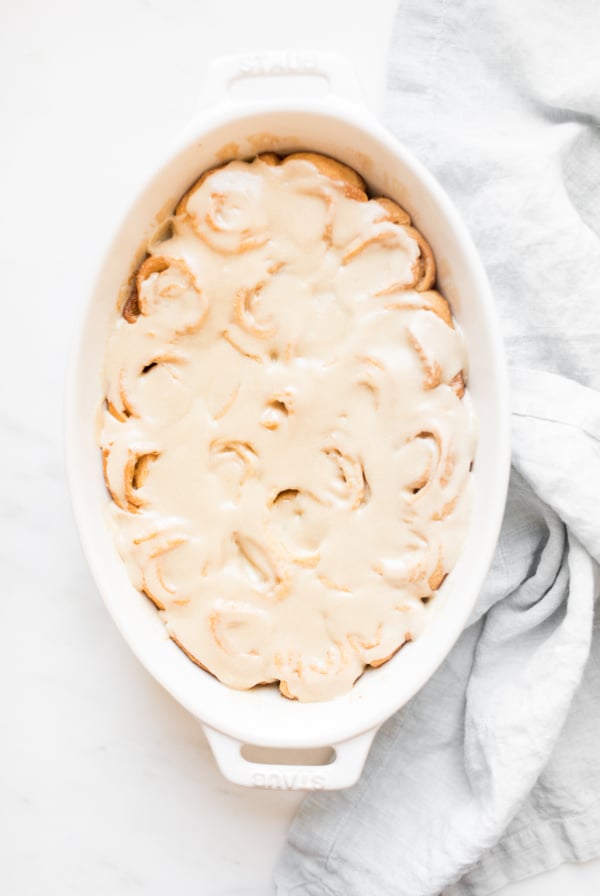 A cinnamon roll topped with caramel sauce in a white dish.