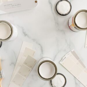 A marble countertop with paint swatches and small cans of open cream paint colors.