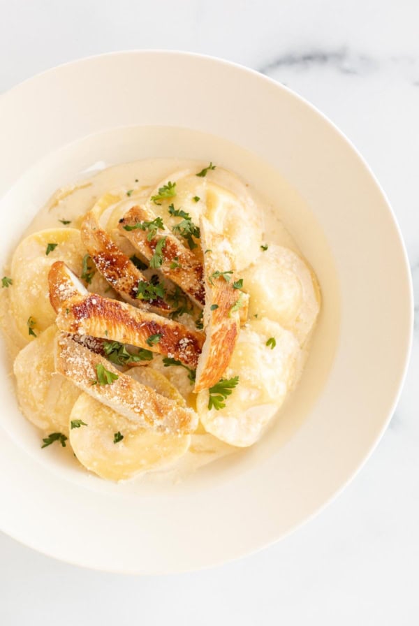 A bowl of chicken pasta garnished with parsley, viewed from above on a white surface.