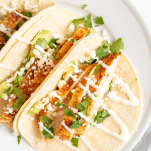 Chicken tacos in corn tortillas on a white surface.