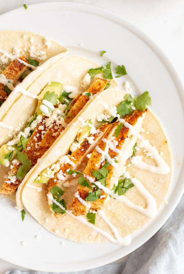 Chicken tacos in corn tortillas on a white surface.