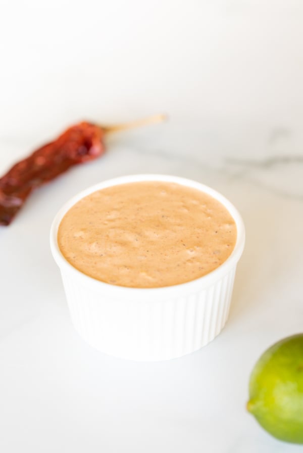 A white bowl of chipotle mayo with chipotle pepper in background.