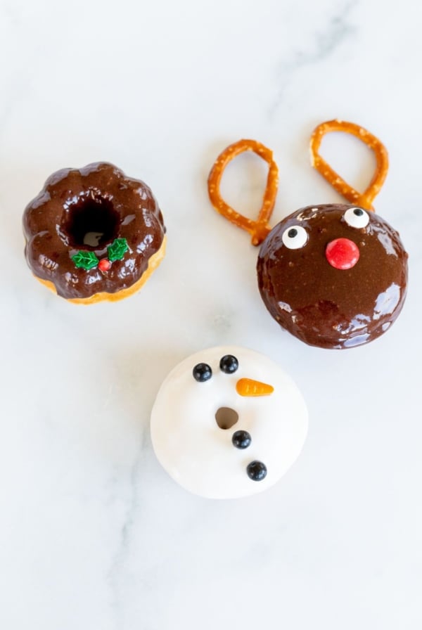 Three cute Christmas donuts on a marble countertop.