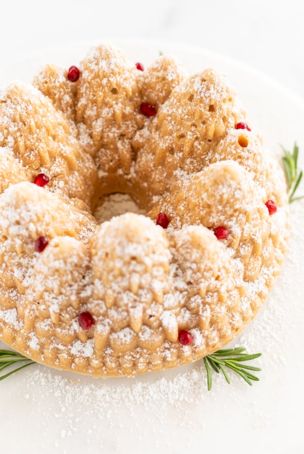 A cinnamon pound cake topped with powdered sugar and a sprig of rosemary.