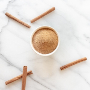 A jar of cinnamon sugar, cinnamon sticks scattered around.