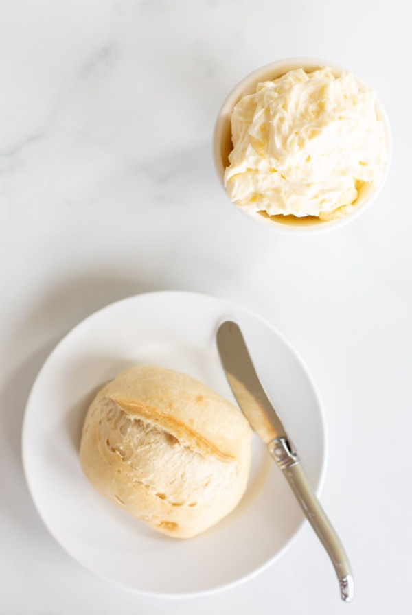 A dinner roll on a white plate with a bowl of garlic butter to the side.