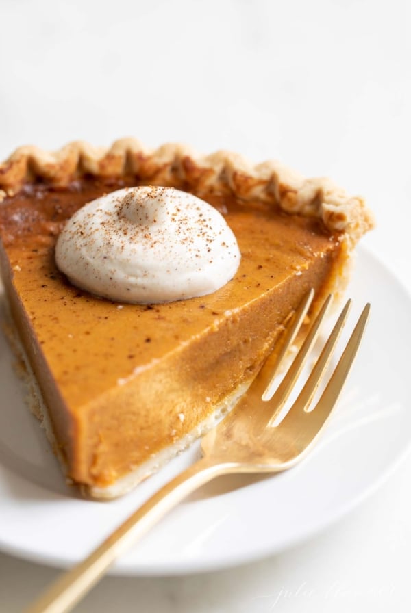 A slice of pumpkin pie with a dollop of eggnog whipped cream on top.