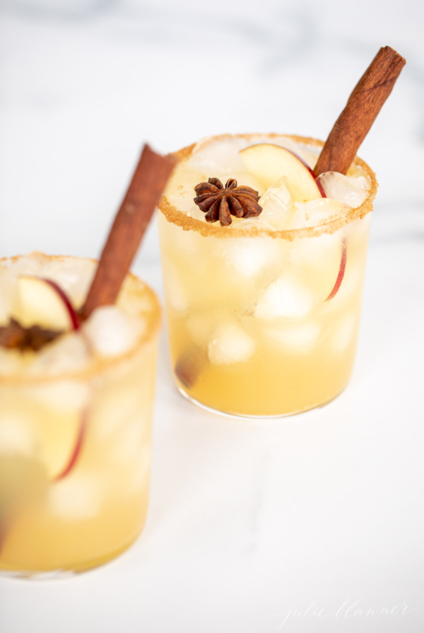 Two glasses of fall apple margarita with cinnamon sticks.