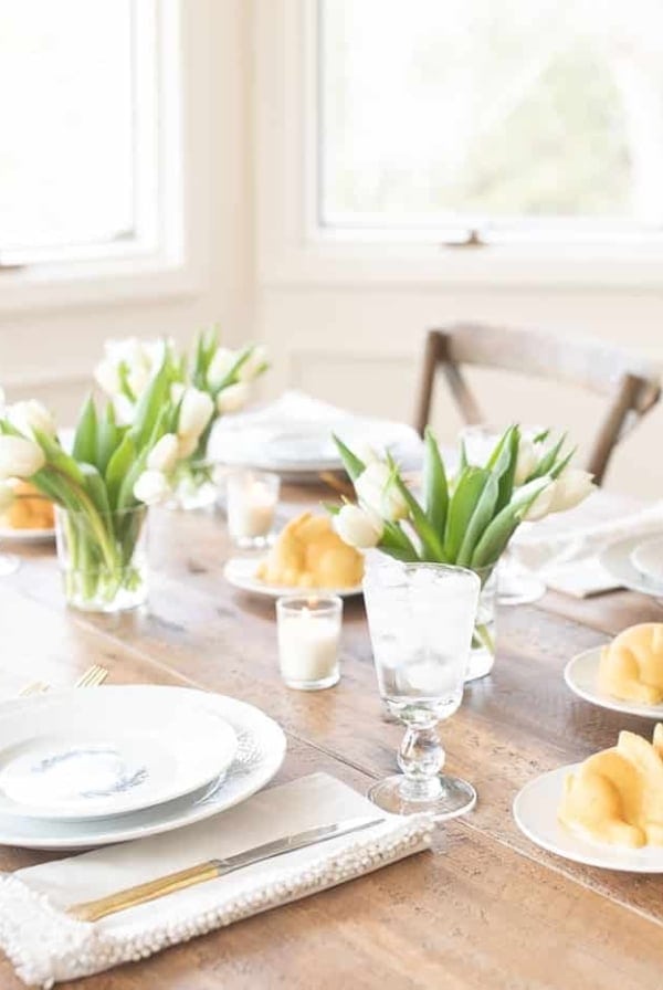 A wooden table filled with miniature Easter cakes and tulips for Easter Flowers