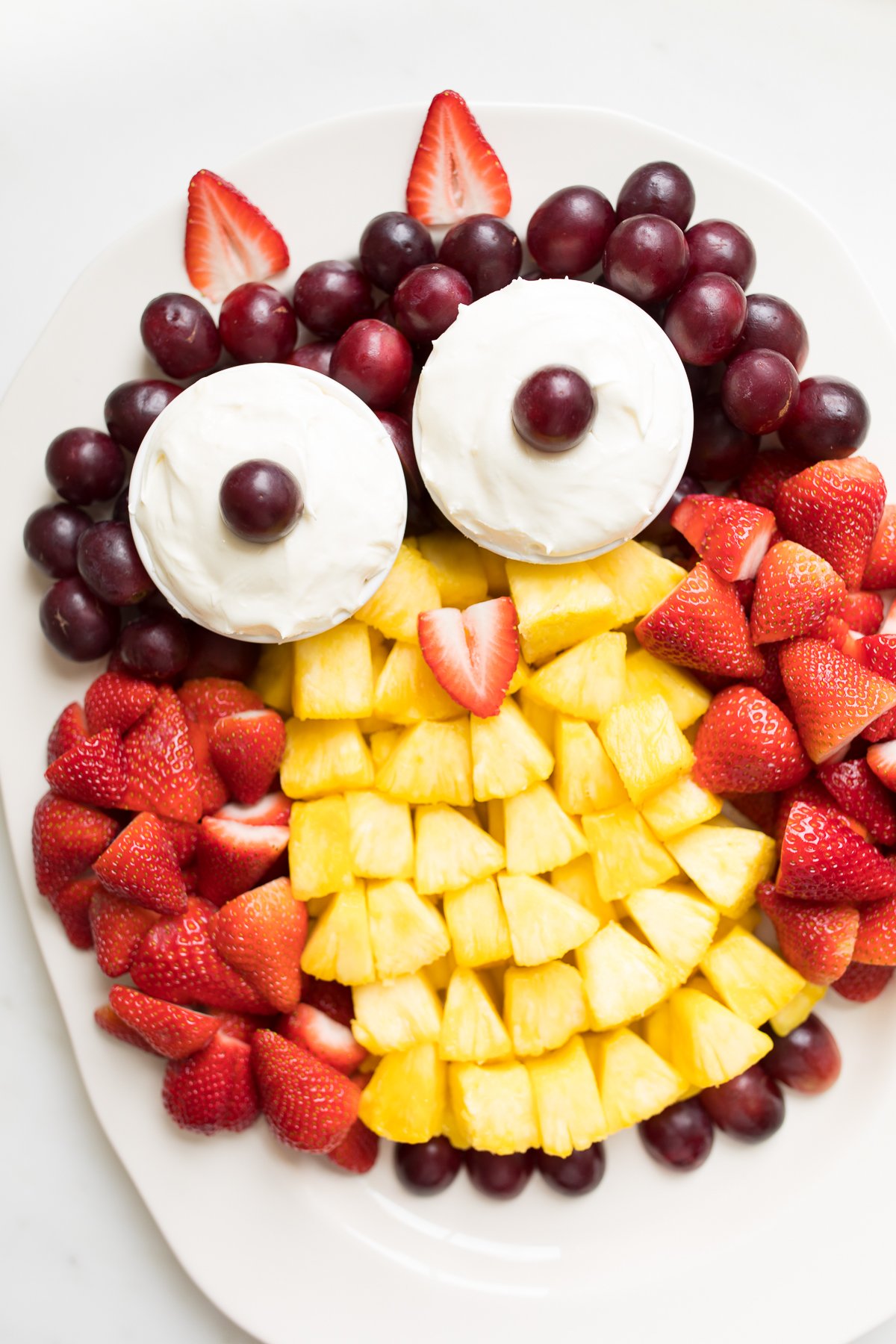 A fruit tray shaped into an owl, featuring cream cheese fruit dip as the owl's eyes.