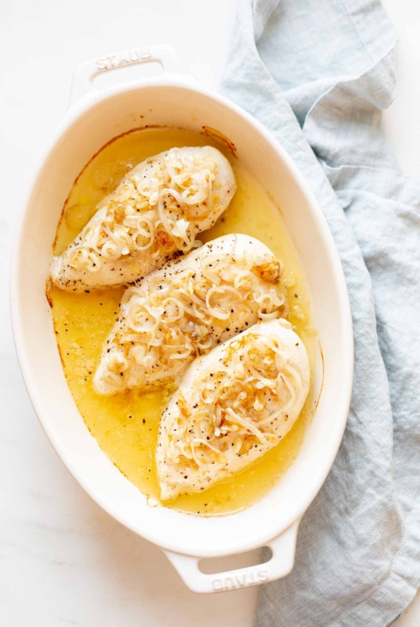 A white oval baking dish, filled with garlic chicken with shallots in a light sauce.