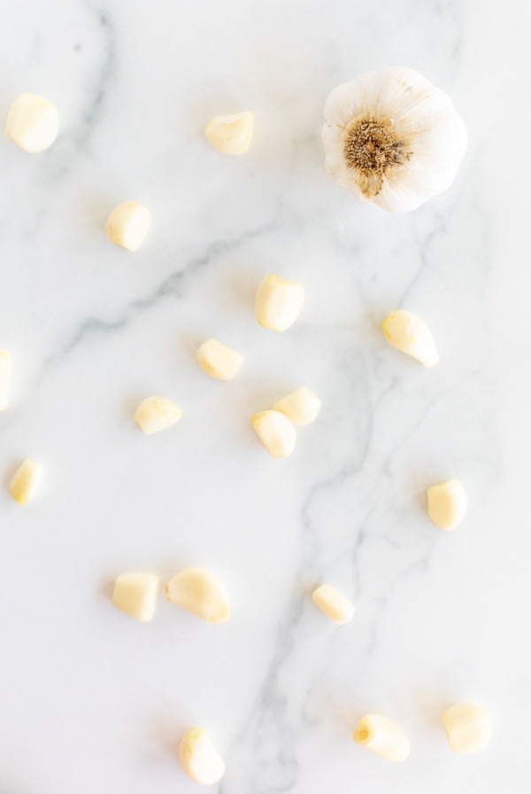 A single head of garlic and more garlic cloves open onto a marble countertop.