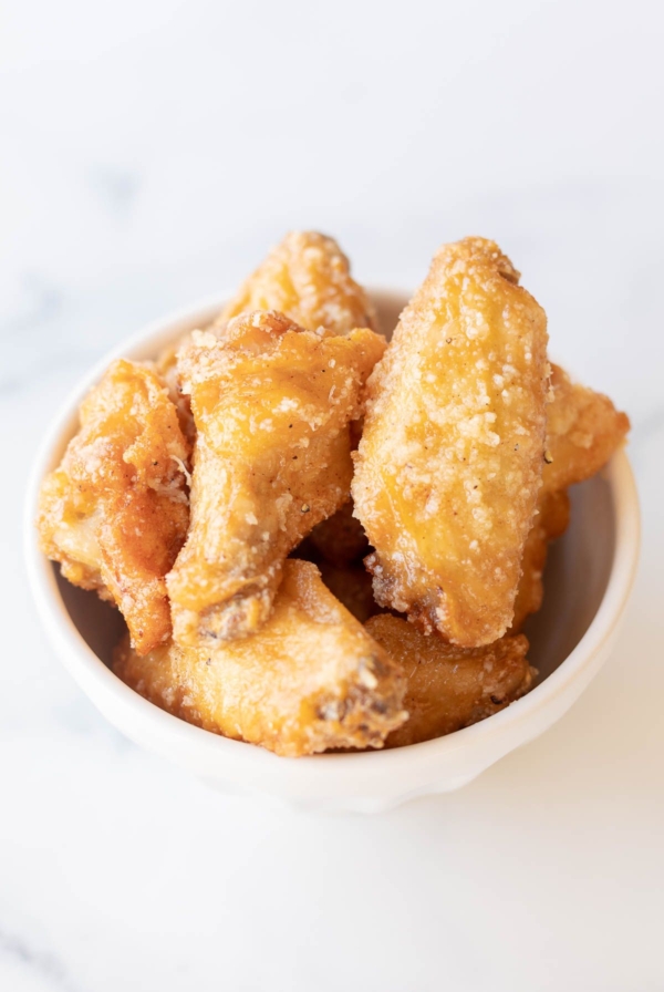 A white bowl filled with garlic parmesan wings, on a marble countertop