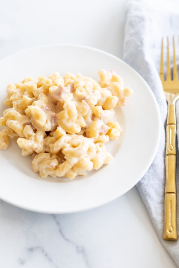 Gouda mac and cheese on a white plate with a gold fork to the side.