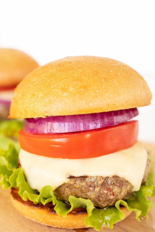 A hamburger stacked with lettuce, tomato, cheese and red onion.