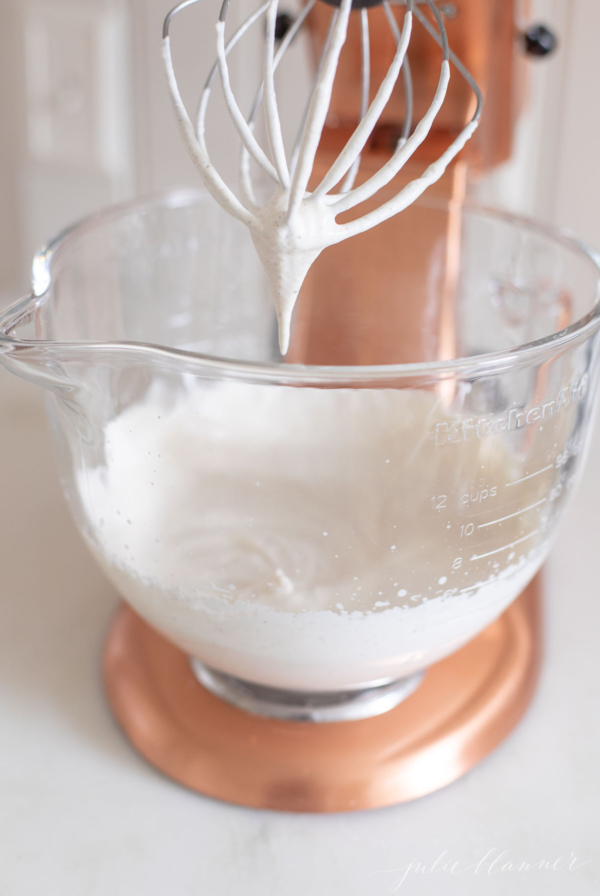 A clear glass mixing bowl of a stand mixer filled with whipped cream.