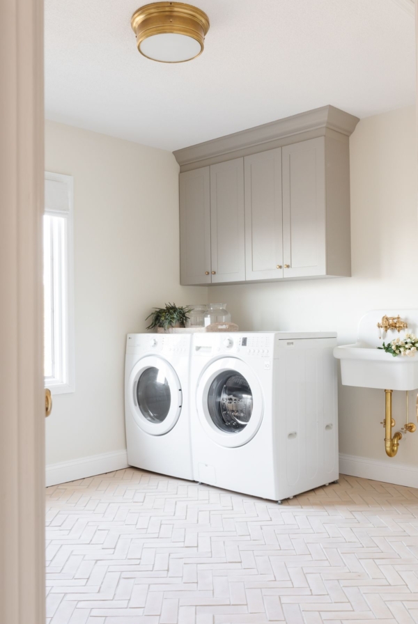 A laundry room with greige cabinets, a wall sink and herringbone floor.