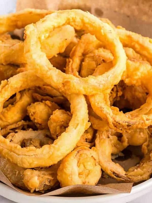 A white bowl of homemade onion rings, butcher paper lining the bowl.