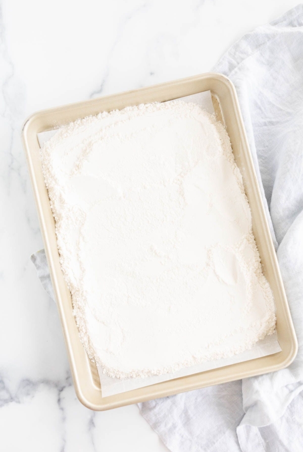 Flour spread out on a gold rimmed baking sheet, on a marble countertop