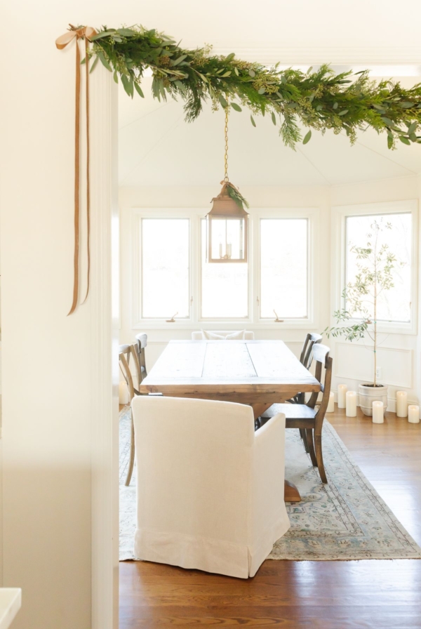 A fresh greenery garland over the entry into a white dining room.