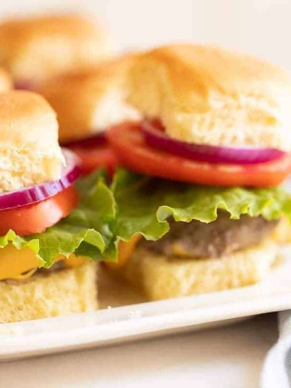 Burgers stacked with lettuce, tomato and onion on a white platter. #burgersintheoven