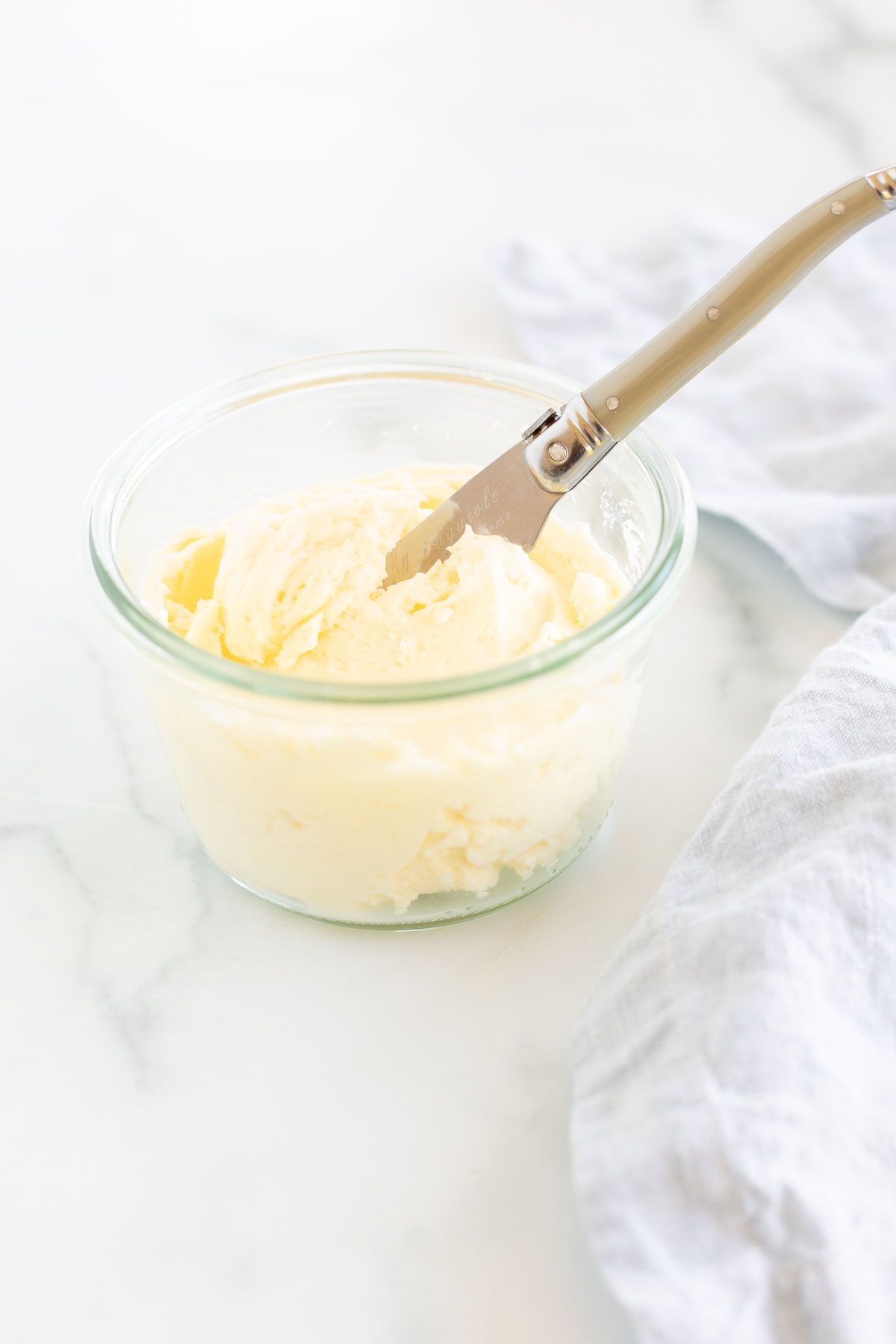 A knife placed over a small glass bowl of homemade butter