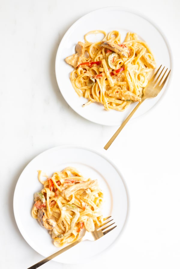 Two white plates of pasta, with gold forks.