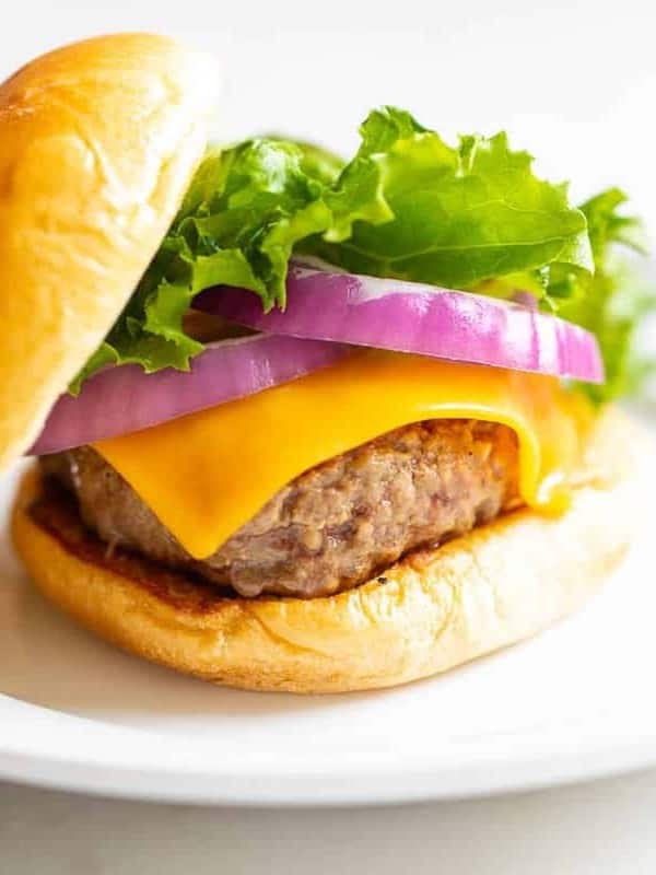 White plate with a cast iron burger stacked with lettuce, red onions and cheese.