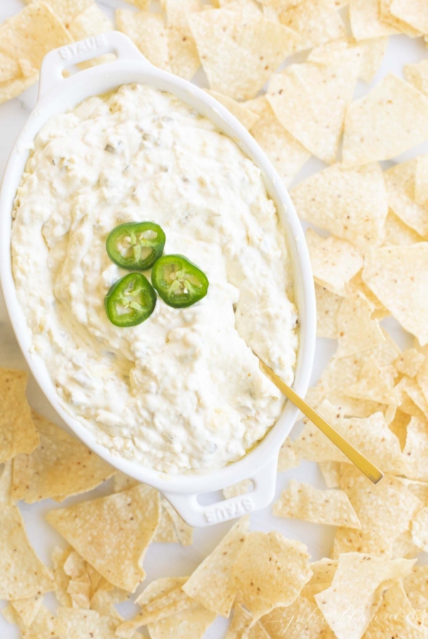 An oval serving dish full of jalapeno dip, surrounded by tortilla chips.