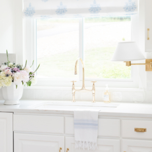 A white kitchen with a brass bridge kitchen faucet over the sink.