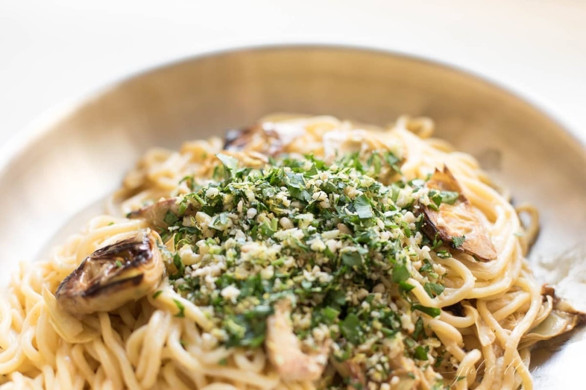 spaghetti in a skillet with artichokes topped with gremolata