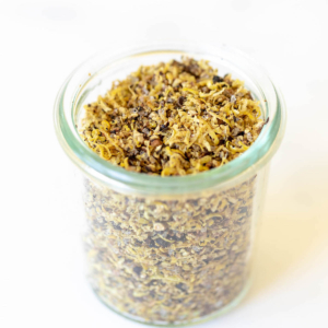 A glass jar on a marble surface, filled with lemon pepper seasoning blend.