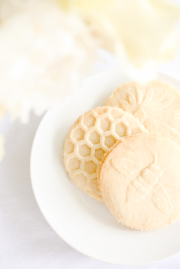 lemon shortbread cookies stamped with flowers, bees and beehives on a white plate