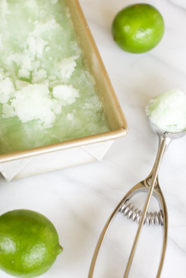 Homemade lime sorbet in a gold loaf pan. A lime and an ice cream scooper are nearby.