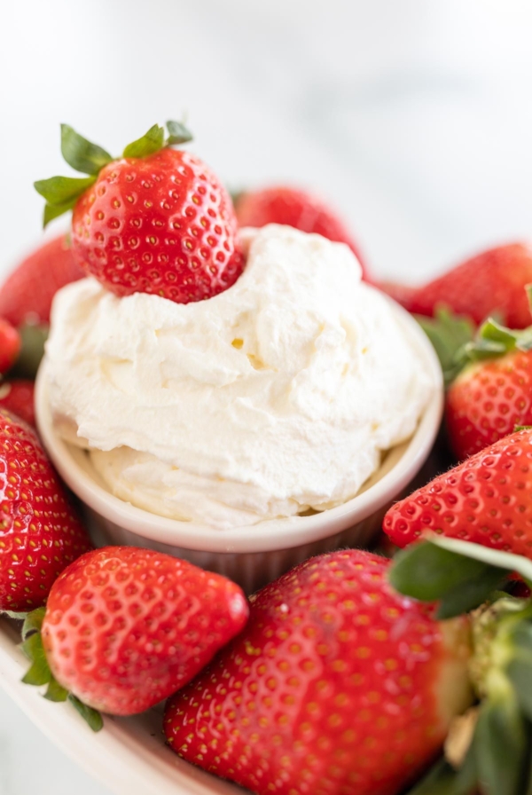 A white plate full of strawberries and a bowl of mascarpone dip in the center.